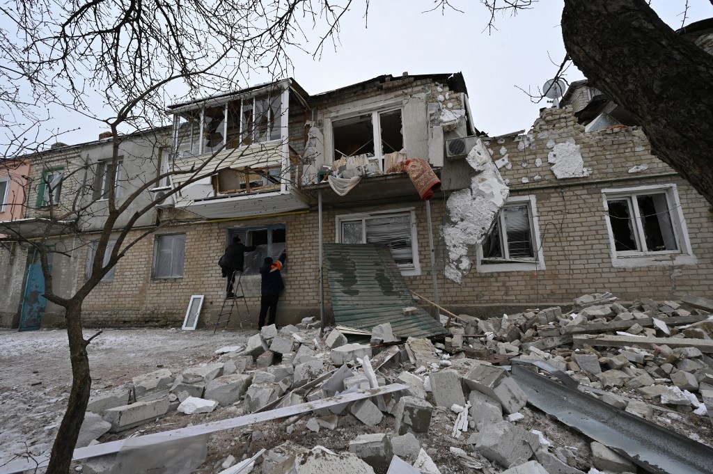 Moradores locais usam lonas plásticas para cobrir uma janela quebrada no prédio residencial de dois andares onde vivem, depois que ela foi parcialmente destruída por bombardeios em Kupiansk, região de Kharkiv — Foto: SERGEY BOBOK / AFP - 13/02/2023