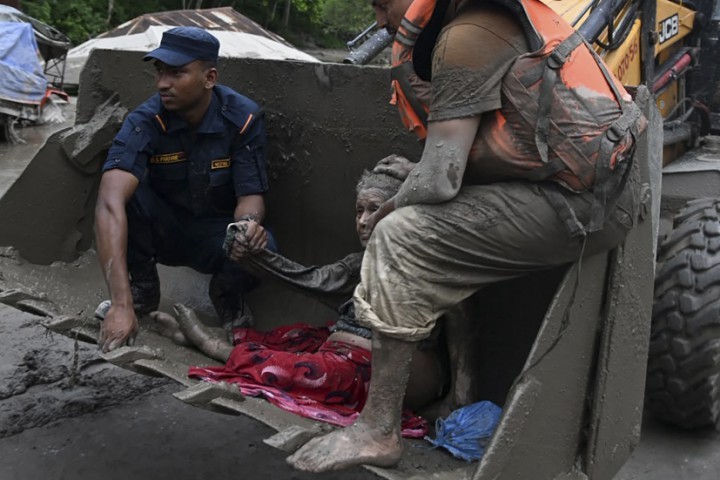 Equipes de resgate usam uma escavadeira para transportar uma pessoa afetada por inundações repentinas em Devghat, no distrito de Nuwakot, no Nepal, em 26 de agosto de 2026 — Foto: Prakash MATHEMA / AFP
