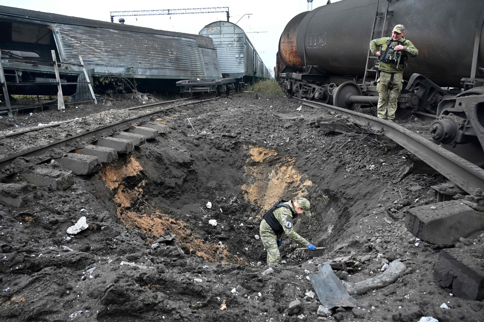 Perito em explosivos examina a cratera de uma explosão de mísseis em uma estação ferroviária de carga em Kharkiv, na Ucrânia — Foto: SERGEY BOBOK / AFP