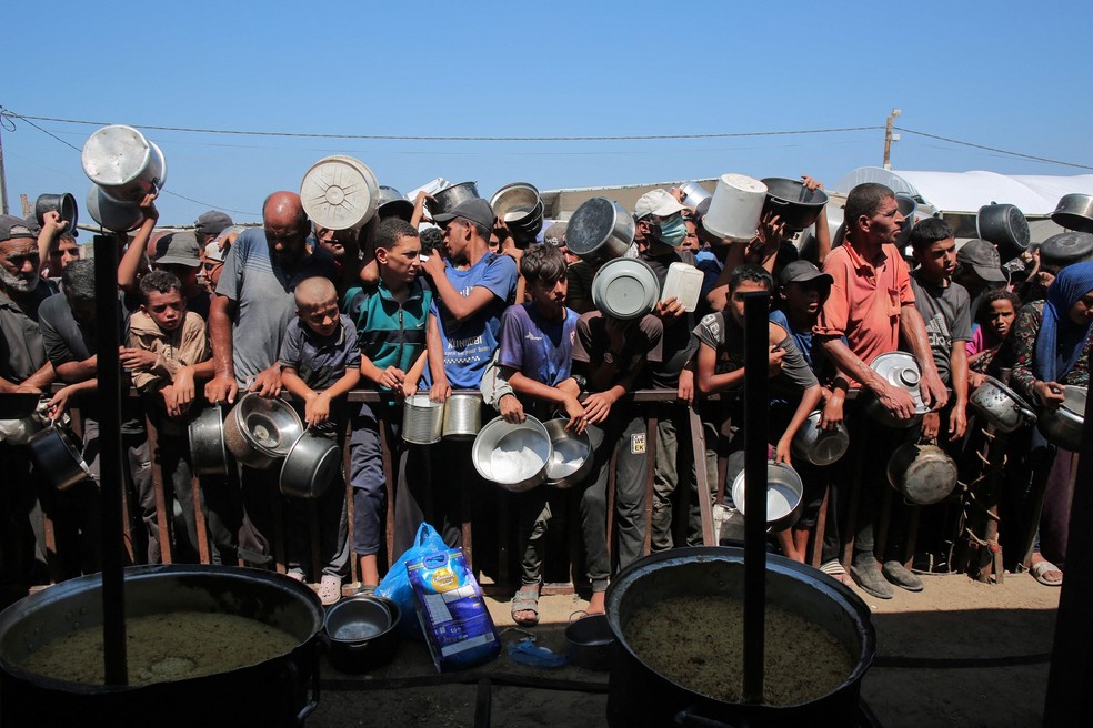 Palestinos aguardam para receber porções de comida de uma cozinha beneficente em Khan Yunis, no sul da Faixa de Gaza — Foto: AFP