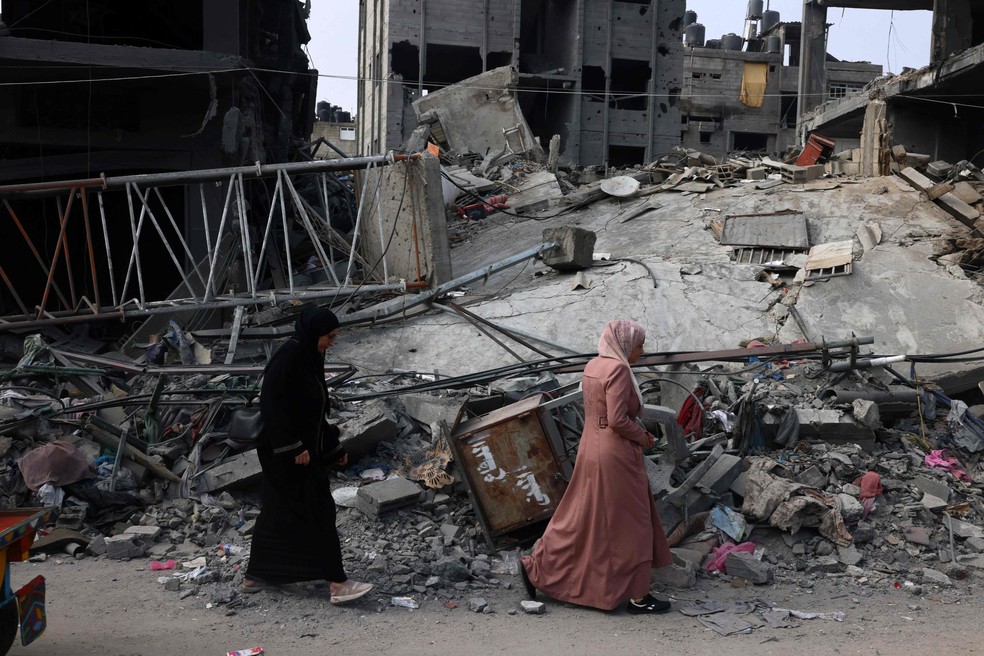 Mulheres caminham diante de escombros de prédio destruído por bombardeios em Rafah, na Faixa de Gaza — Foto: Said Khatib / AFP