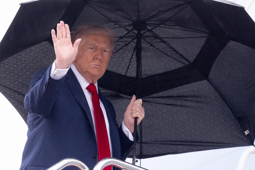 O presidente dos EUA, Donald Trump, segura um guarda-chuva enquanto acena ao embarcar no Air Force One — Foto: SAUL LOEB/AFP
