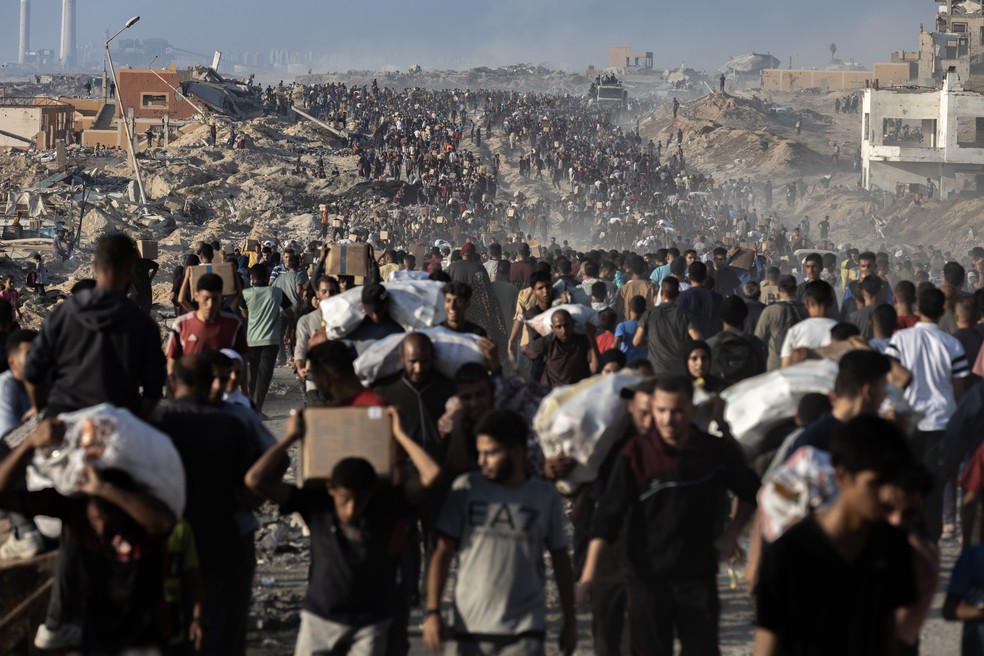 Palestinos carregam pacotes de alimentos doados enquanto outros correm em direção a um ponto de distribuição na Cidade de Gaza — Foto: Saher Alghorra/The New York Times