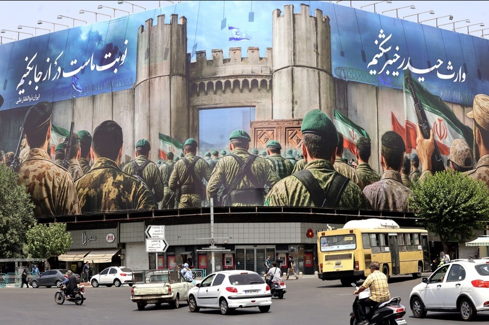 Veículos passam em frente a um enorme banner na Praça Enghelab, em Teer. Mídia iraniana informou que um ataque noturno israelense no norte do país matou nove pessoas, pouco antes do anúncio do presidente dos EUA sobre o início de um cessar-fogo entre Israel e Irã — Foto: Atta Kenare/AFP