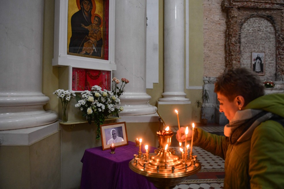 Uma fiel acende uma vela em frente a um retrato do Papa Francisco em igreja, em São Petersburgo, em 21 de abril de 2025. — Foto: Olga Maltseva / AFP