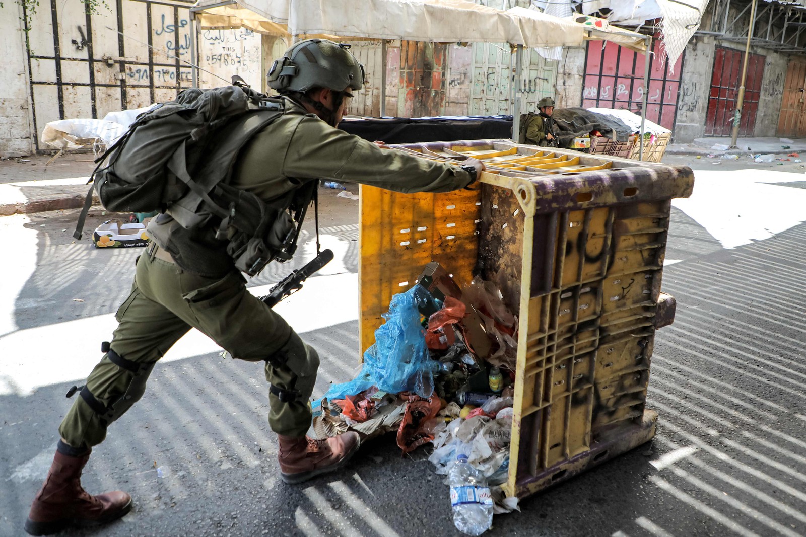 Um soldado israelense derruba uma lixeira para se proteger durante confrontos no centro de Hebron — Foto: MOSAB SHAWER / AFP