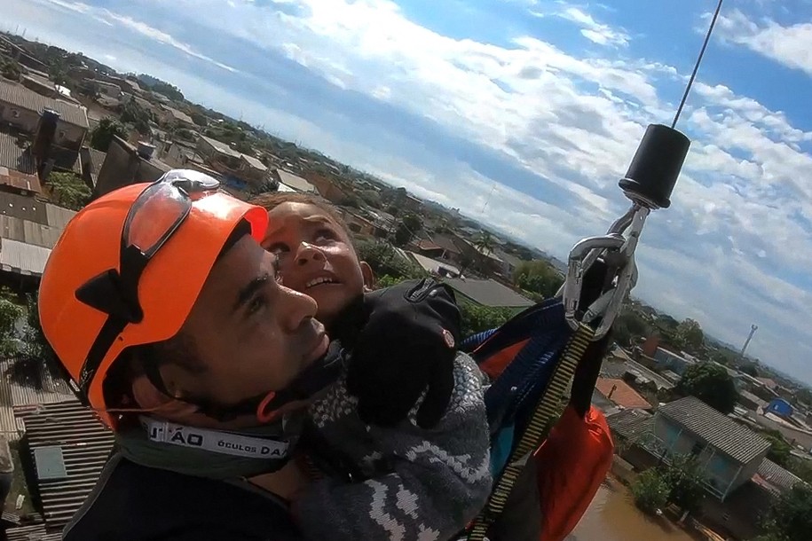 Capturada de um vídeo divulgado pela Marinha do Brasil, em 5 de maio de 2024, mostra resgate de uma criança, por helicóptero, no bairro Mathias Velho, em Canoas, Rio Grande do Sul. De cima a baixo, equipes de resgate vasculham edifícios em Porto Alegre em busca de habitantes presos em apartamentos ou em telhados. — Foto: MARINHA DO BRASIL / AFP