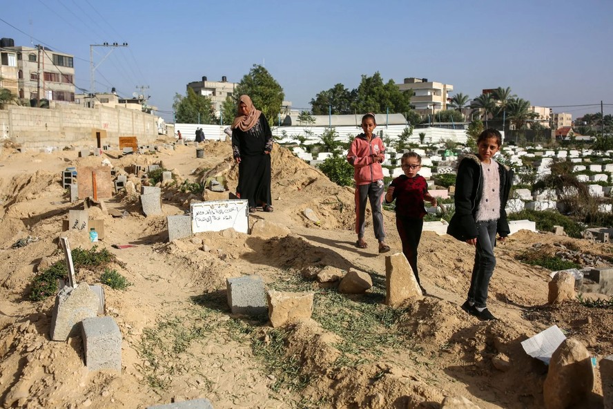 Mulher e filhas procuram em um cemitério os túmulos de parentes durante uma trégua em novembro no centro da Faixa de Gaza