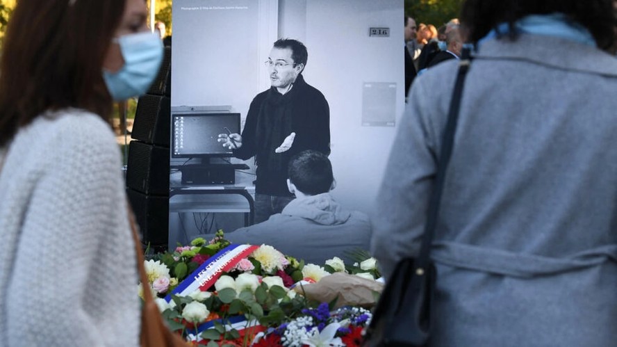 Pessoas diante de uma fotografia que mostra o professor de história e geografia francesa Samuel Paty em uma cerimônia de homenagem realizada um ano após a morte de Paty em Eragny-sur-Oise, noroeste de Paris, em 16 de outubro de 2021