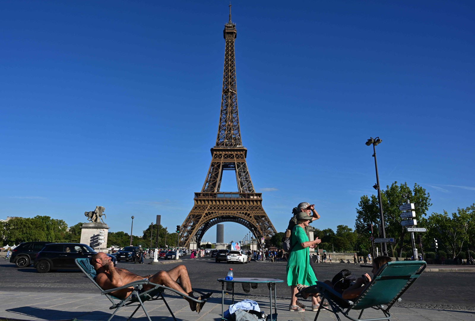 Pessoas tomam banho de sol diante da Torre Eiffel, em Paris, em 21 de agosto de 2023. — Foto: Miguel MEDINA / AFP