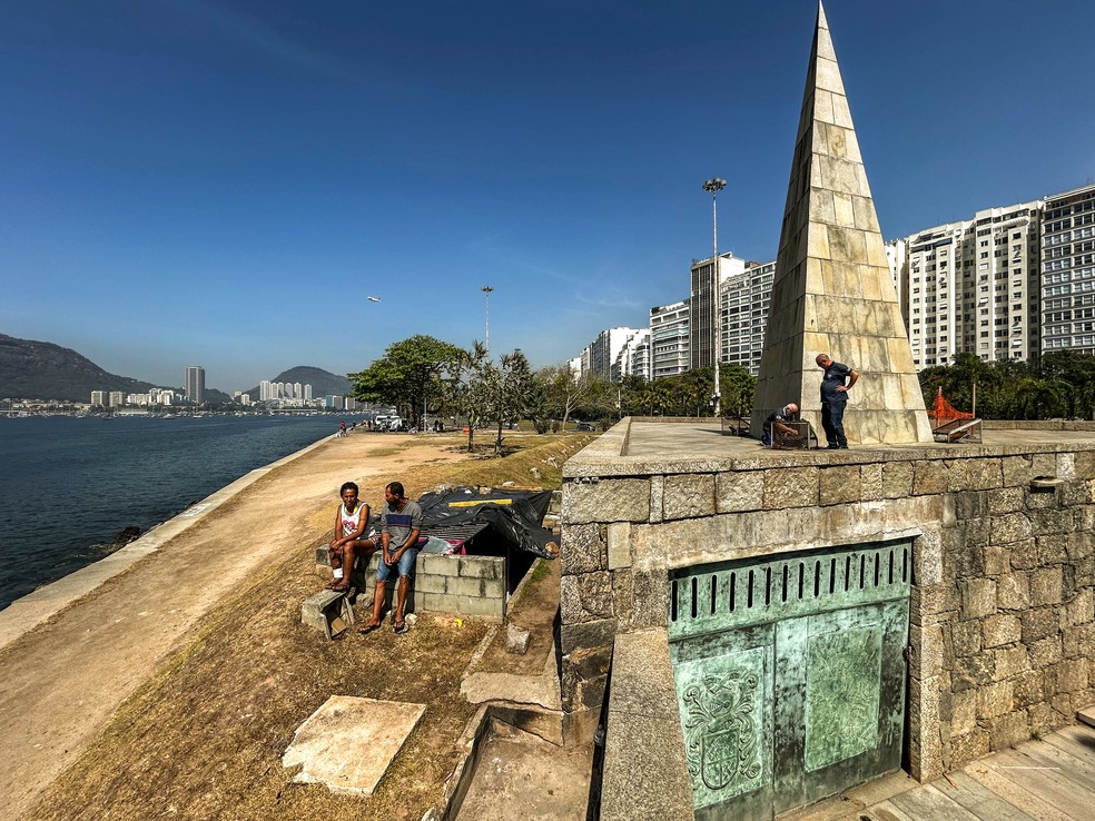 Técnicos da Rioluz trabalham nos refletores, enquanto Andreza e Vitor estão sentados sob o Monumento a Estácio de Sá — Foto: Gabriel de Paiva / Agência O Globo