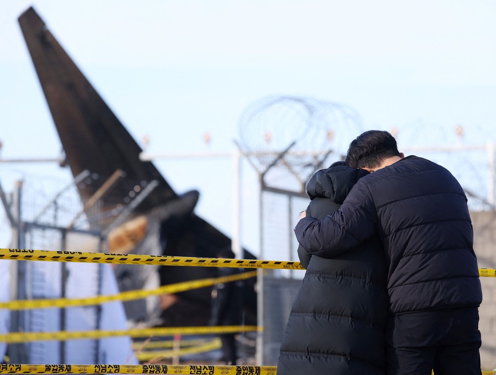 Parentes de vítimas do acidente com avião da Jeju Air, na Coreia do Sul, diante dos destroços da aeronave — Foto: YONHAP / AFP