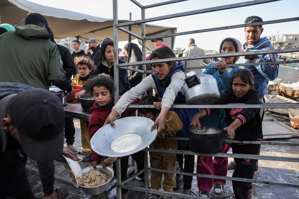 Moradores da Cidade de Gaza levam panelas para receber alimentos doados durante o mês sagrado do Ramadã — Foto: BASHAR TALEB / AFP
