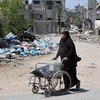 Mulher empurra cadeira de rodas na Cidade de Gaza - AFP