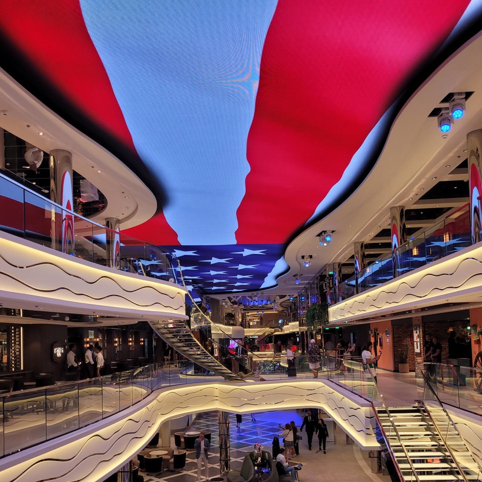 Uma bandeira dos Estados Unidos é projetada no teto da World Galleria, a via central do navio de cruzeiros MSC World America — Foto: Eduardo Maia / O Globo