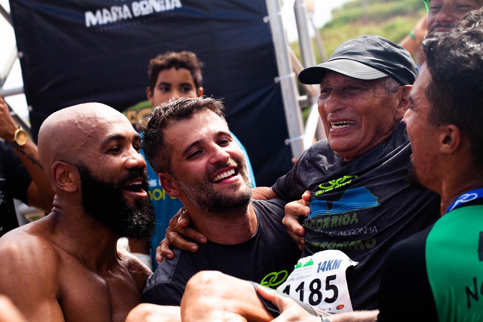 Seu Renê Jerônimo é carregado por Bruno Gagliasso: corrida em Fernando de Noronha ganhou patrocínio da Olympikus com ajuda do ator — Foto: Divulgação Olympikus