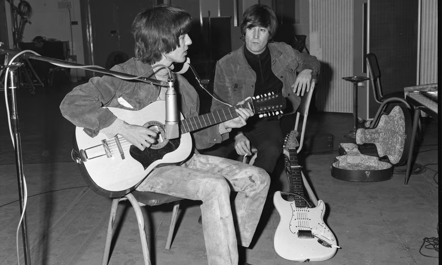 George Harrison toca o violão Framus Hootenanny de 12 cordas de John Lennon, que o observa