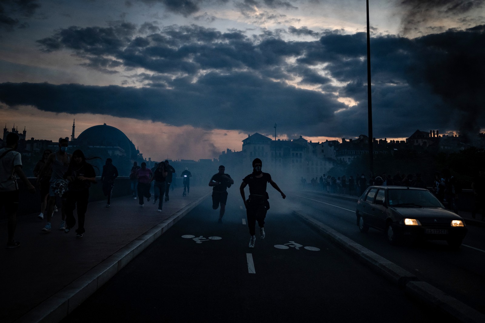 Manifestantes correm de bombas de gás lacrimogêneo lançadas durante confrontos com a polícia em Lyon — Foto: JEFF PACHOUD / AFP