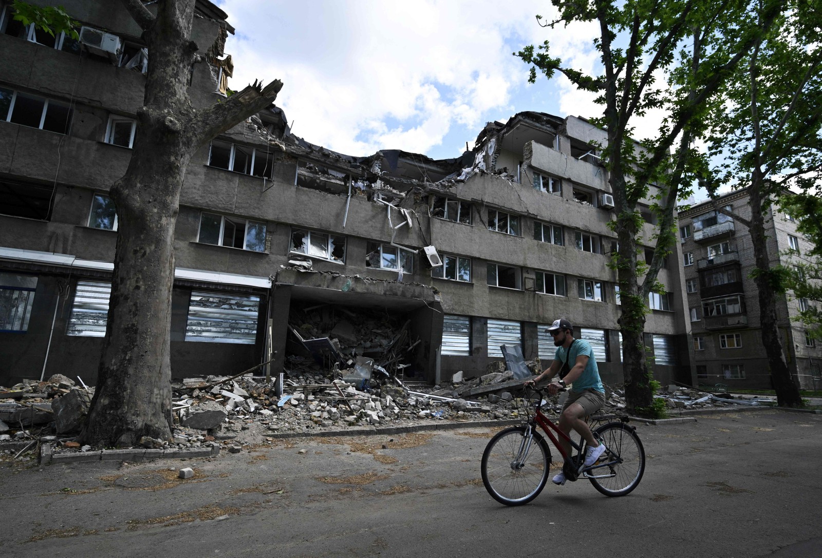 Homem passa de bicicleta por um prédio do hotel Ingul, destruído por um ataque aéreo russo em março, na cidade de Mykolaiv, no sul da Ucrânia — Foto: GENYA SAVILOV / AFP