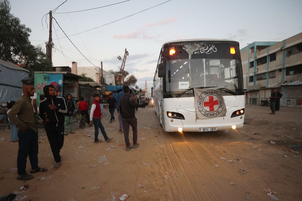 Jovens palestinos observam um ônibus com o emblema da Cruz Vermelha Internacional se deslocar em direção ao leste da Faixa de Gaza, vindo de Khan Younis — Foto: Omar al-Qattaa/AFP