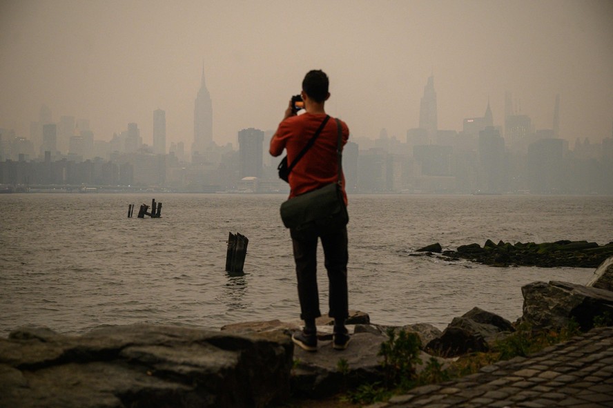 Homem observa a cidade de Nova York coberta por uma névoa cinza após incêndios no Canadá