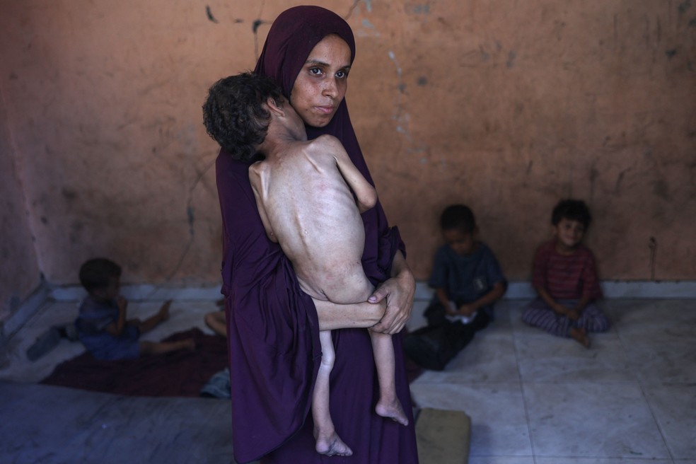 Fome em Gaza: Naeema, palestina de 30 anos, carrega o filho Yazan, de 2 — Foto: Omar Al-Qattaa / AFP