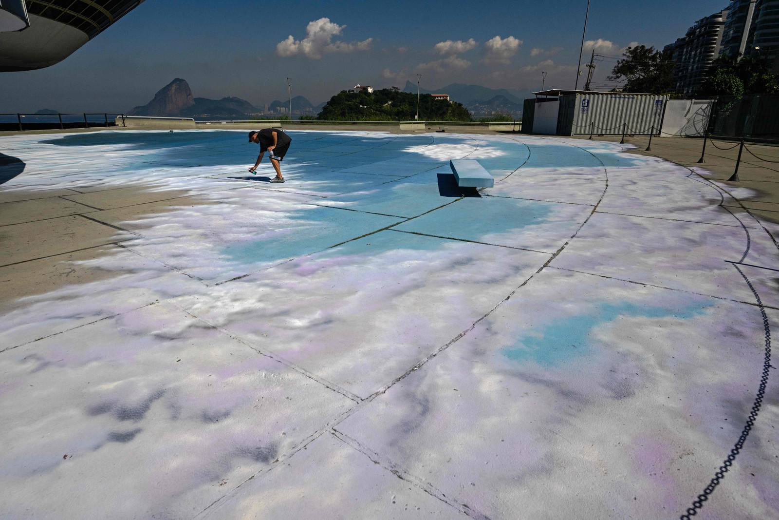Artista ajuda a criar um design de nuvens concebido pelo grafiteiro brasileiro Toz no chão do Museu de Arte Contemporânea — Foto: Carl de Souza/AFP