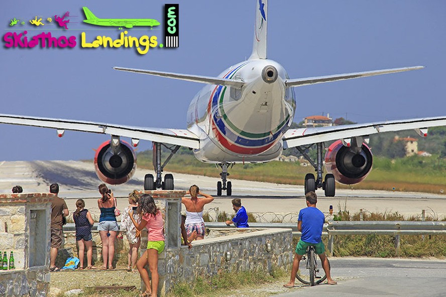 Decolagem da pista 02 do aeroporto de Skiathos. Pessoas esperam para tirar fotos e gravar vídeos enquanto o avião se prepara para levantar voo