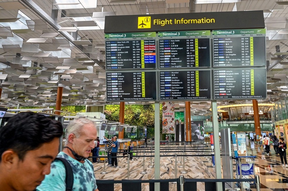 Pessoas passam por um painel de embarque exibindo o voo SQ318 da Singapore Airlines para Londres Heathrow como cancelado no Aeroporto Changi de Cingapura, em Cingapura — Foto: Roslan RAHMAN / AFP