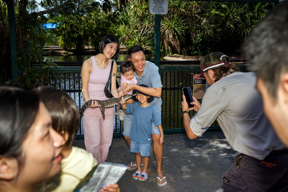 Uma família posa para uma foto com um crocodilo jovem no Parque Crocodylus, uma atração turística em Darwin — Foto: Matthew Abbott / The New York Times