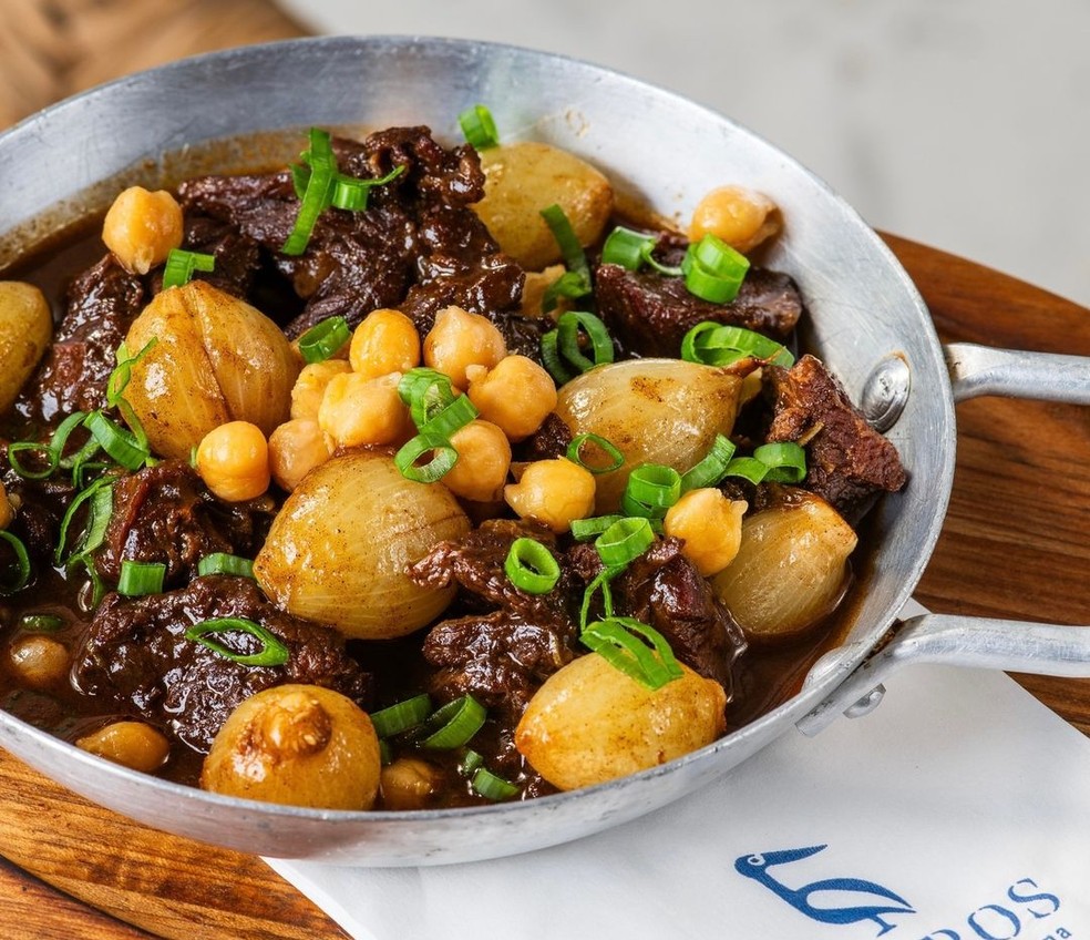 Petros Greek Taverna: O stifado traz carne temperada à moda grega, com especiarias, cebolas caramelizadas e grão-de-bico — Foto: Reprodução
