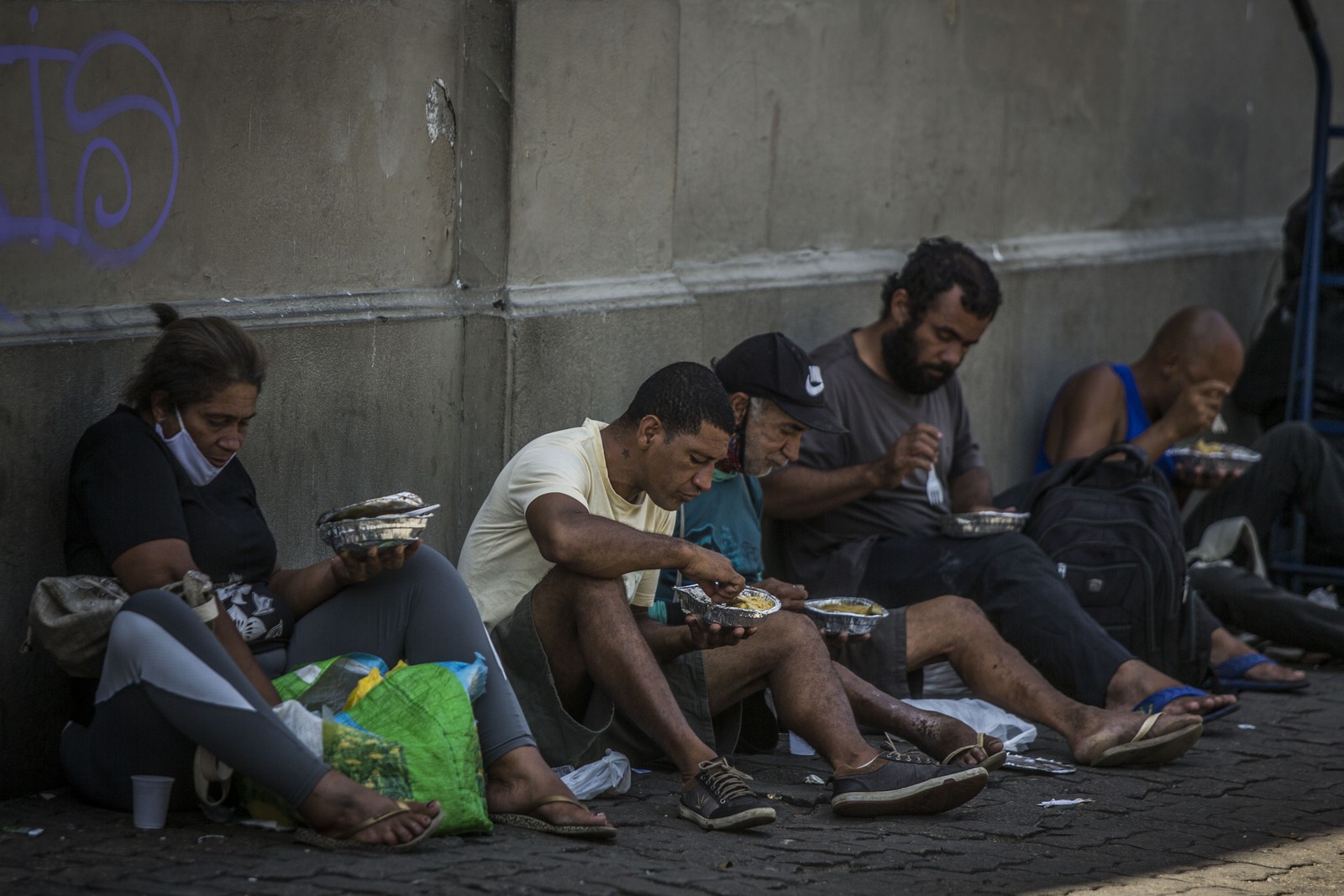 Pessoas que receberam refeição se sentam à sombra, na calçada, para comer no Centro do RioAgência O Globo