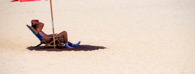 Banhista encontra sombra sob um guarda-sol em Rehoboth Beach, em Delaware, EUA, em 28 de julho de 2023. Serviço Nacional de Meteorologia anunciou "calor opressivo" durante todo o fim de semana  — Foto: Jim WATSON / AFP