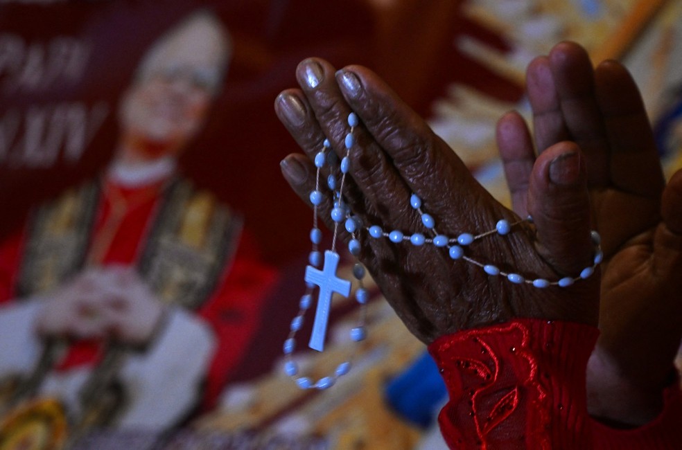 Uma mulher reza ao lado da imagem de Robert Francis Prevost, que se tornou Papa Leão XIV em 8 de maio de 2025, em frente à catedral de Chiclayo, no norte do Peru — Foto: ERNESTO BENAVIDES / AFP