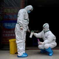 Médico em traje de proteção desinfeta colega em clínica de teste para Covid-19 em Wuhan, na China — Foto: Noel Celis / AFP