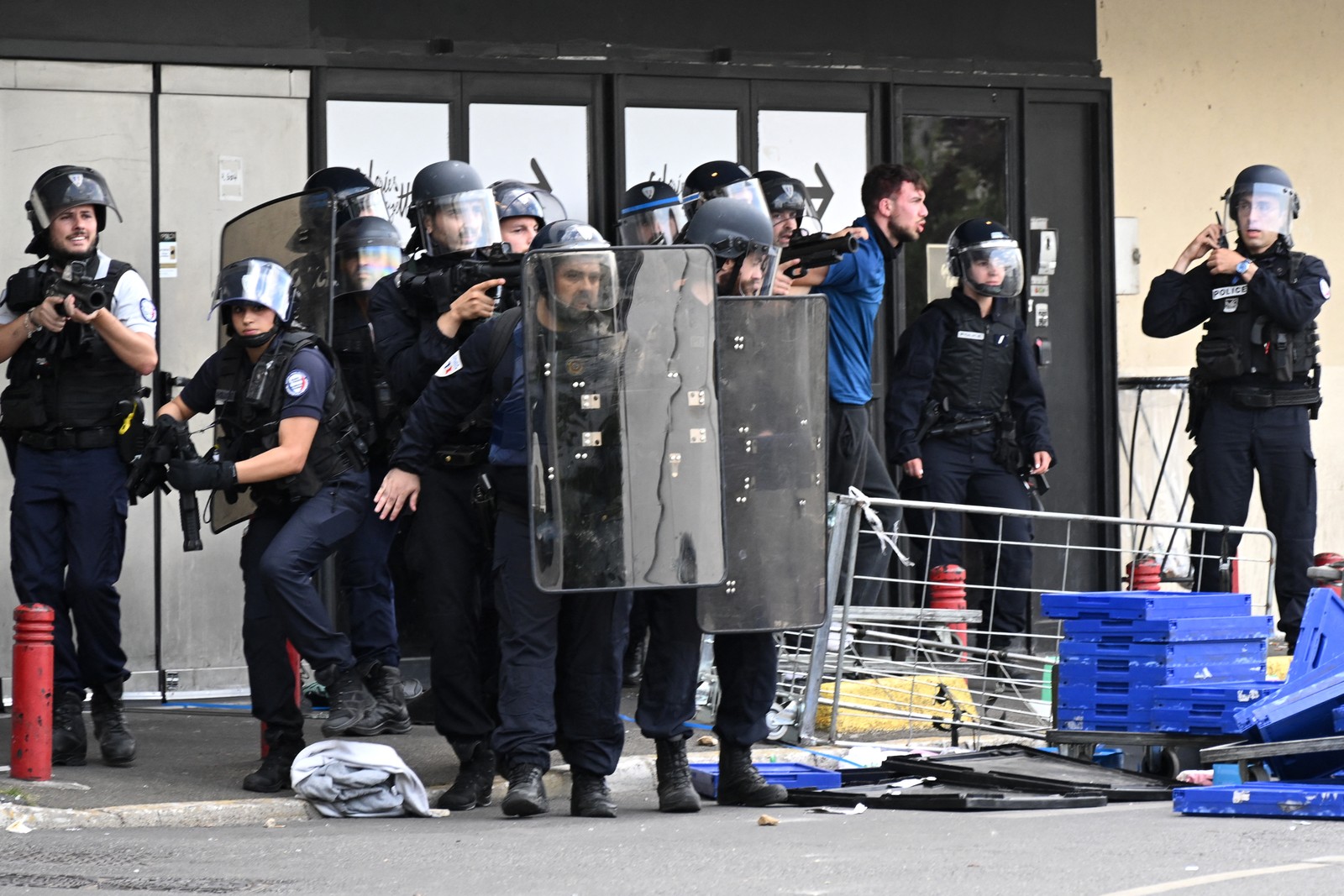 Policiais detêm um manifestante (R) e fazem guarda em frente ao shopping Rosny 2 em Rosny-sous-Bois, nos subúrbios orientais de Paris, em 30 de junho de 2023, durante distúrbios que eclodiram após o tiroteio de um motorista adolescente pela polícia francesa em um subúrbio de Paris em 27 de junho. O presidente francês, Emmanuel Macron, anunciou medidas que incluem mais policiais e pediu aos pais que mantenham os menores fora das ruas, enquanto luta para conter os distúrbios noturnos por causa do tiro fatal de um adolescente por um policial em uma parada de trânsito.  — Foto: Bertrand GUAY / AFP