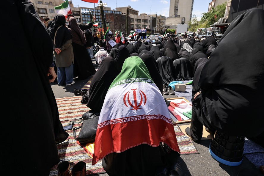 Uma mulher iraniana envolta na bandeira nacional realiza as orações do meio-dia enquanto pessoas se reúnem na Praça da Revolução de Teerã, após os Estados Unidos e o Irã concordarem com um cessar-fogo de duas semanas