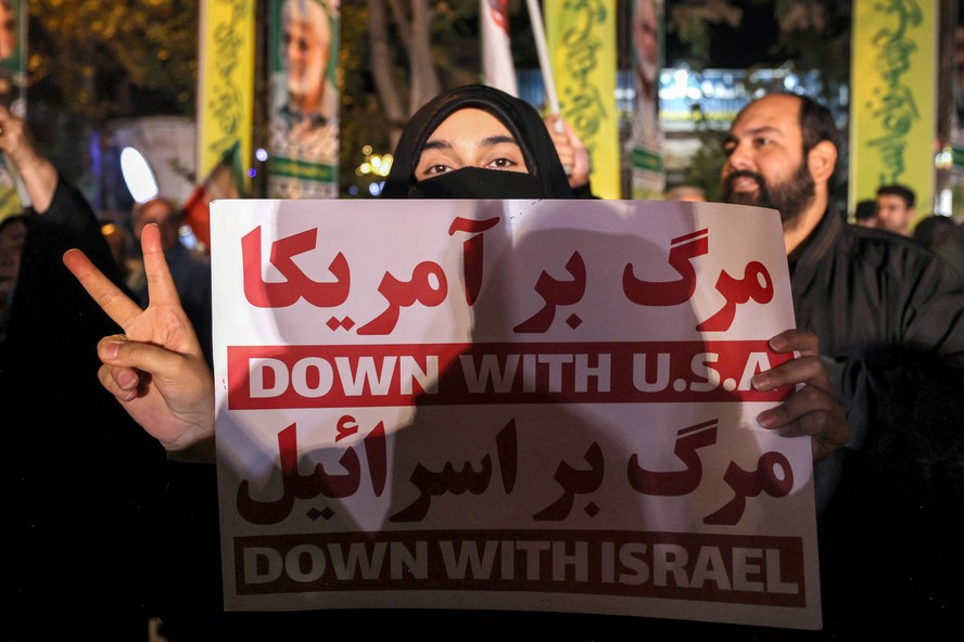 Mulher com cartaz contra Israel e EUA participa de ato a favor do regime na Praça Palestina, em Teerã, após ataque contra o território israelense