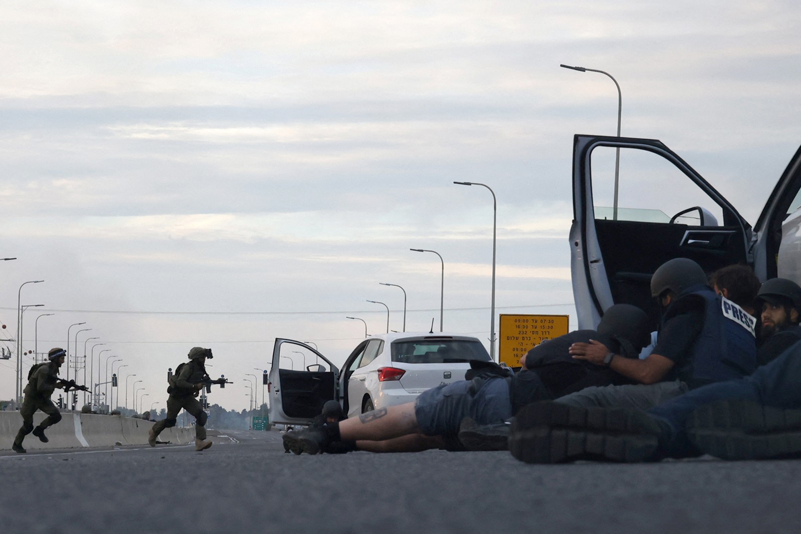 Jornalistas se escondem atrás de carros enquanto soldados israelenses tomam posição durante confrontos com combatentes palestinos perto do Kibutz Gevim — Foto: Oren ZIV / AFP