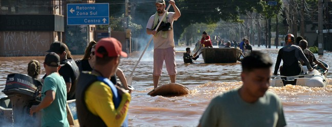 De cima a baixo, equipes de resgate vasculham prédios em Porto Alegre em busca de habitantes presos em apartamentos ou telhados. No centro da foto, homem se locomove na rua inundada com prancha de Stand Up. — Foto: NELSON ALMEIDA / AFP