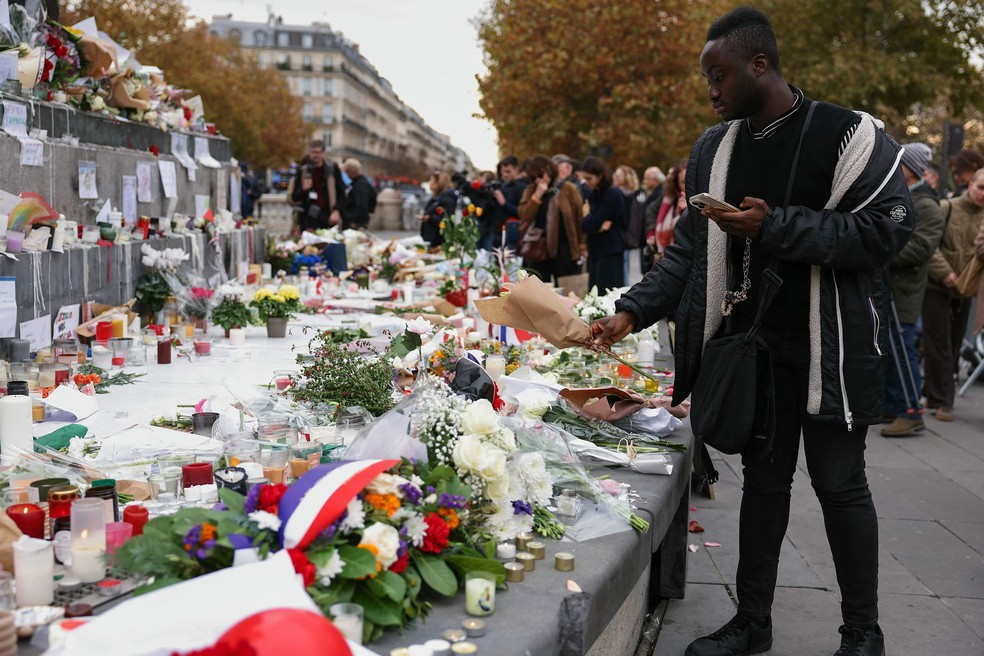 Homem coloca um ramo de flores num memorial improvisado na Place de la Republique, em Paris, durante o aniversário que marca uma década dos ataques terroristas — Foto: THOMAS SAMSON / AFP