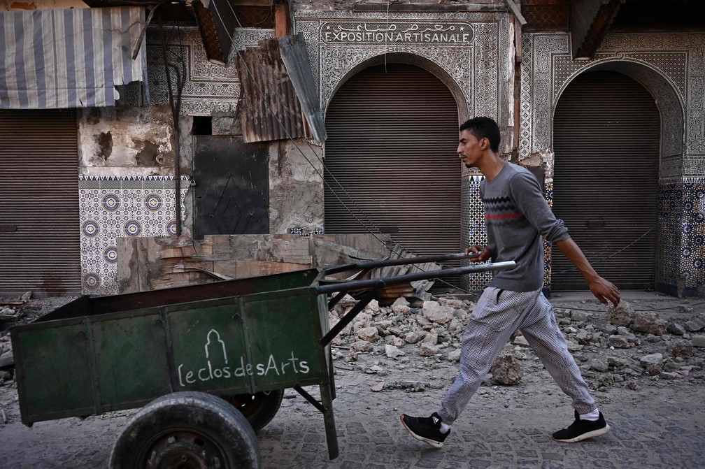 Carregador passa com carrinho em riua por prédios danificados, em Marrakech. — Foto: Philippe Lopez/AFP