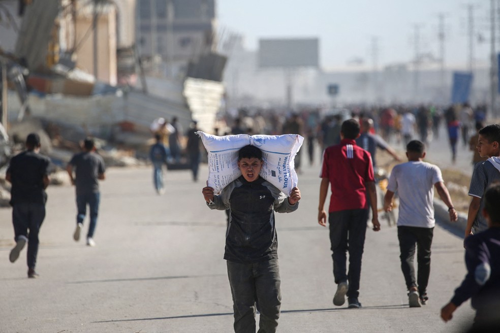Criança palestina carrega saco de alimento em rua de Deir al-Balah, na Faixa de Gaza — Foto: Eyad BABA / AFP