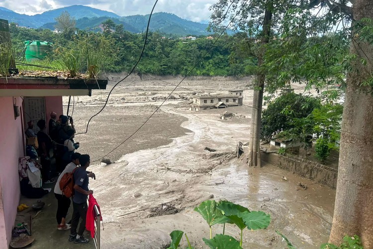 Moradores observam uma torrente de água barrenta avançar por um rio após inundações repentinas no Nepal em 26 de agosto de 2026. — Foto: Prakash MATHEMA / AFP