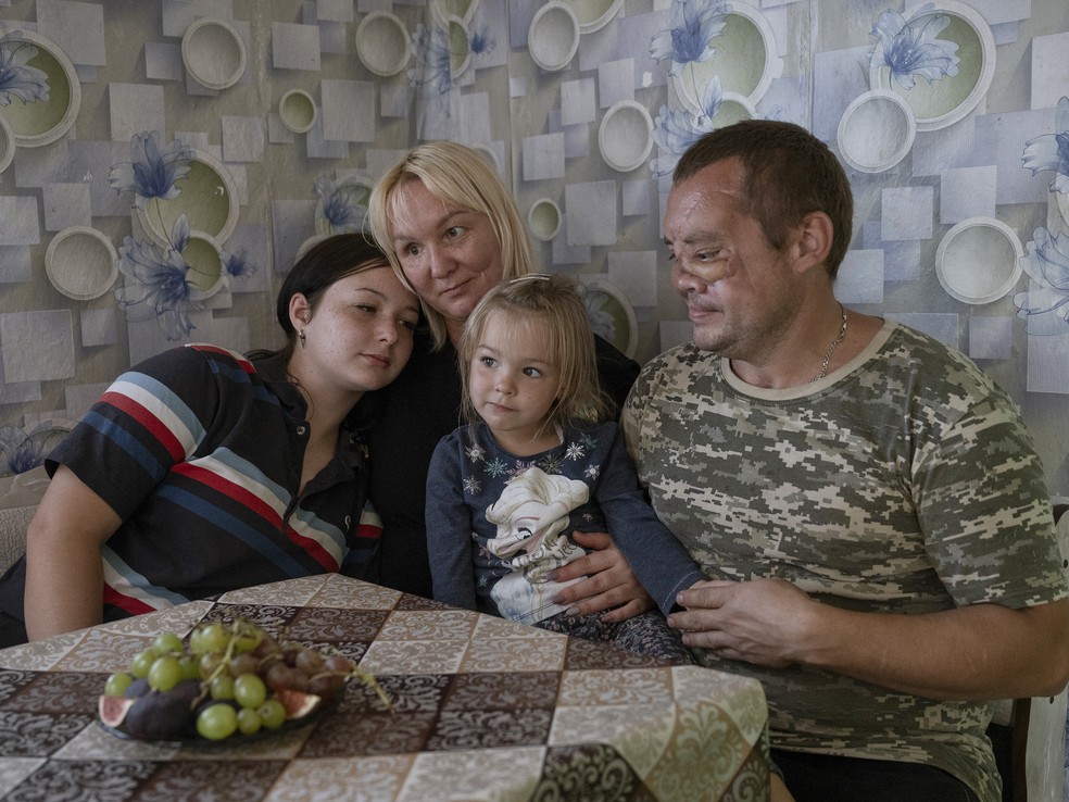Artur Tkachenko, à direita, que ficou gravemente ferido por um míssil russo, com sua esposa, Julia, e seus filhos em casa em Novosofiivka, Ucrânia — Foto: Laetitia Vancon/The New York Times