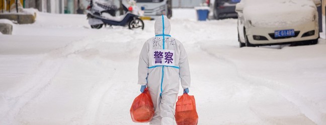 Policial usa equipamento de proteção individual e carrega alimentos para distribuir em área residencial restrita devido à disseminação da Covid-19, em 15 de março de 2022, na Mongólia — Foto: AFP