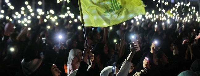 Apoiadores do Hezbollah seguram seus telefones e agitam a bandeira do partido durante uma celebração que marca o 40º aniversário da criação do movimento xiita no subúrbio sul de Beirute  — Foto: ANWAR AMRO / AFP