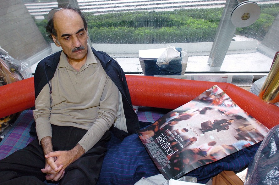 Mehran Karimi Nasseri com o poster do filme 'O Terminal' no aeroporto Charles de Gaulle, Paris, em 2004