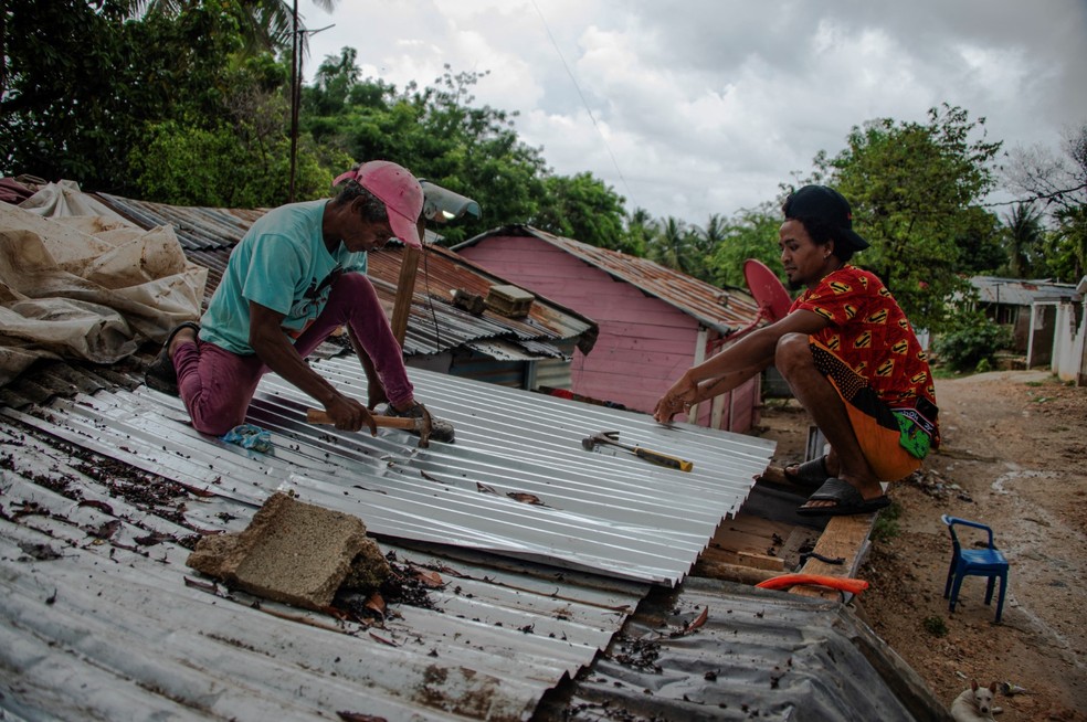 Dois homens consertam o telhado de uma casa após a passagem da tempestade tropical Melissa, antes de se tornar um furacão, em Barahona, na República Dominicana, em 28 de outubro de 2025 — Foto: AFP