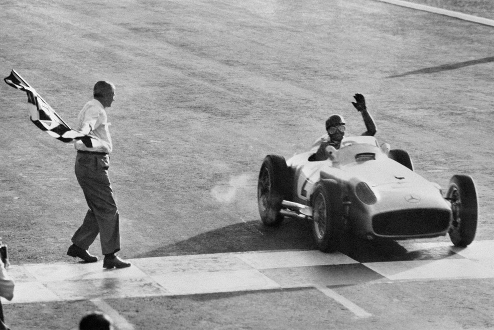 Argentine driver Juan Manuel Fangio, five-time F1 champion, at the wheel of his Mercedes, salutes as he crosses the finish line of the Formula 1 Grand Prix in Buenos Aires, January 16, 1955. — Photo: AFP